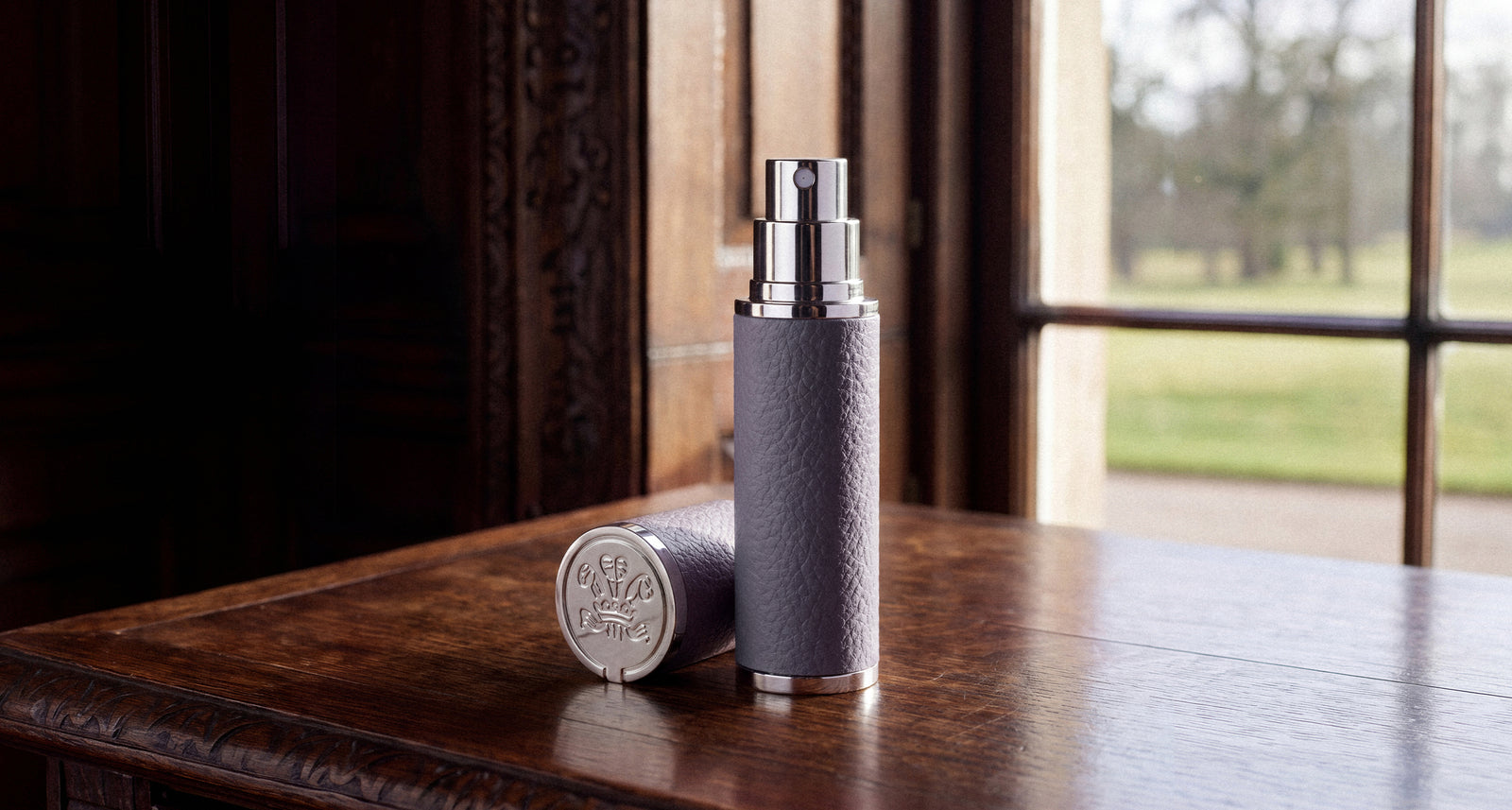A Creed Iris Debonair flacon and travel atomizer on a polished wooden table
